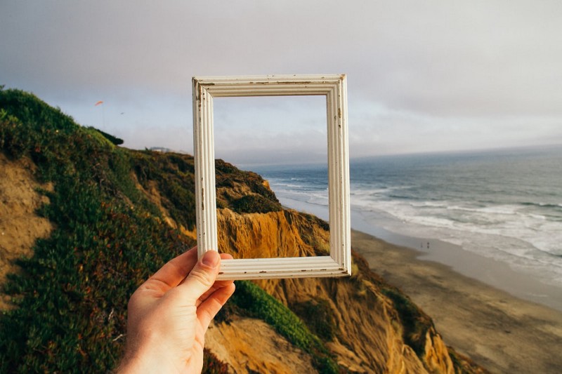 Empty frame being held up with a coastal scene of the cliffs and sand meeting the ocean in the background.